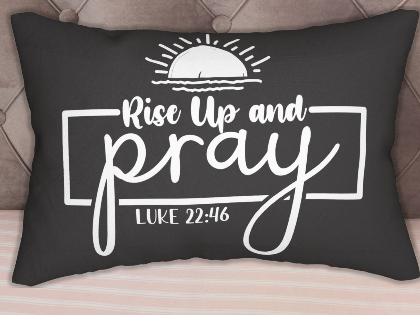 A black throw pillow with white text "Rise Up and Pray" under a sun illustration. Below is "Luke 22:46" in a rectangular frame. The tone is inspirational.