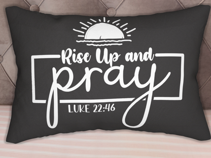 A black throw pillow with white text "Rise Up and Pray" under a sun illustration. Below is "Luke 22:46" in a rectangular frame. The tone is inspirational.