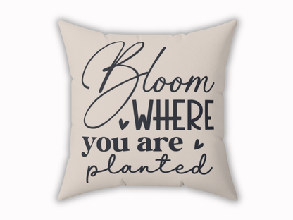 A beige throw pillow features the motivational phrase "Bloom where you are planted" in elegant, navy script. Heart accents add a warm, uplifting tone.