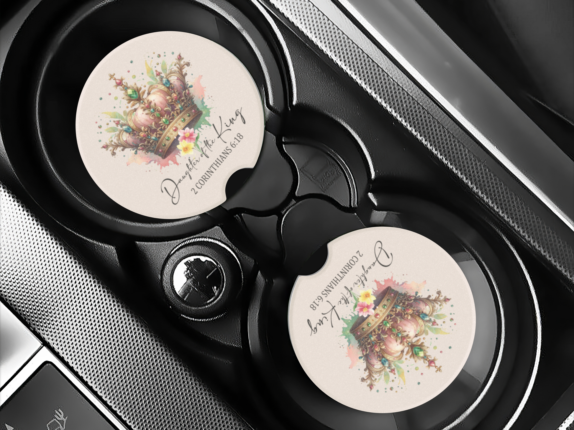 Car cup holder with a decorative coaster featuring a detailed crown illustration, floral accents, and script text reading “Daughter of the King, 2 Corinthians 6:18.”