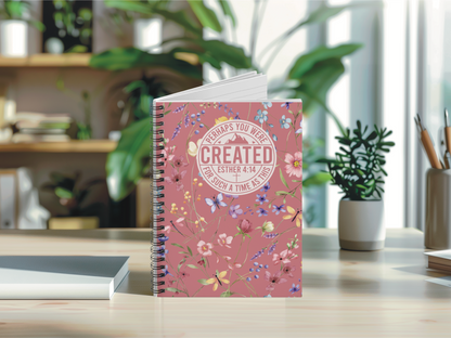 A floral journal with the text "Perhaps You Were Created for Such a Time as This" on a desk, surrounded by plants and books in bright, natural light.