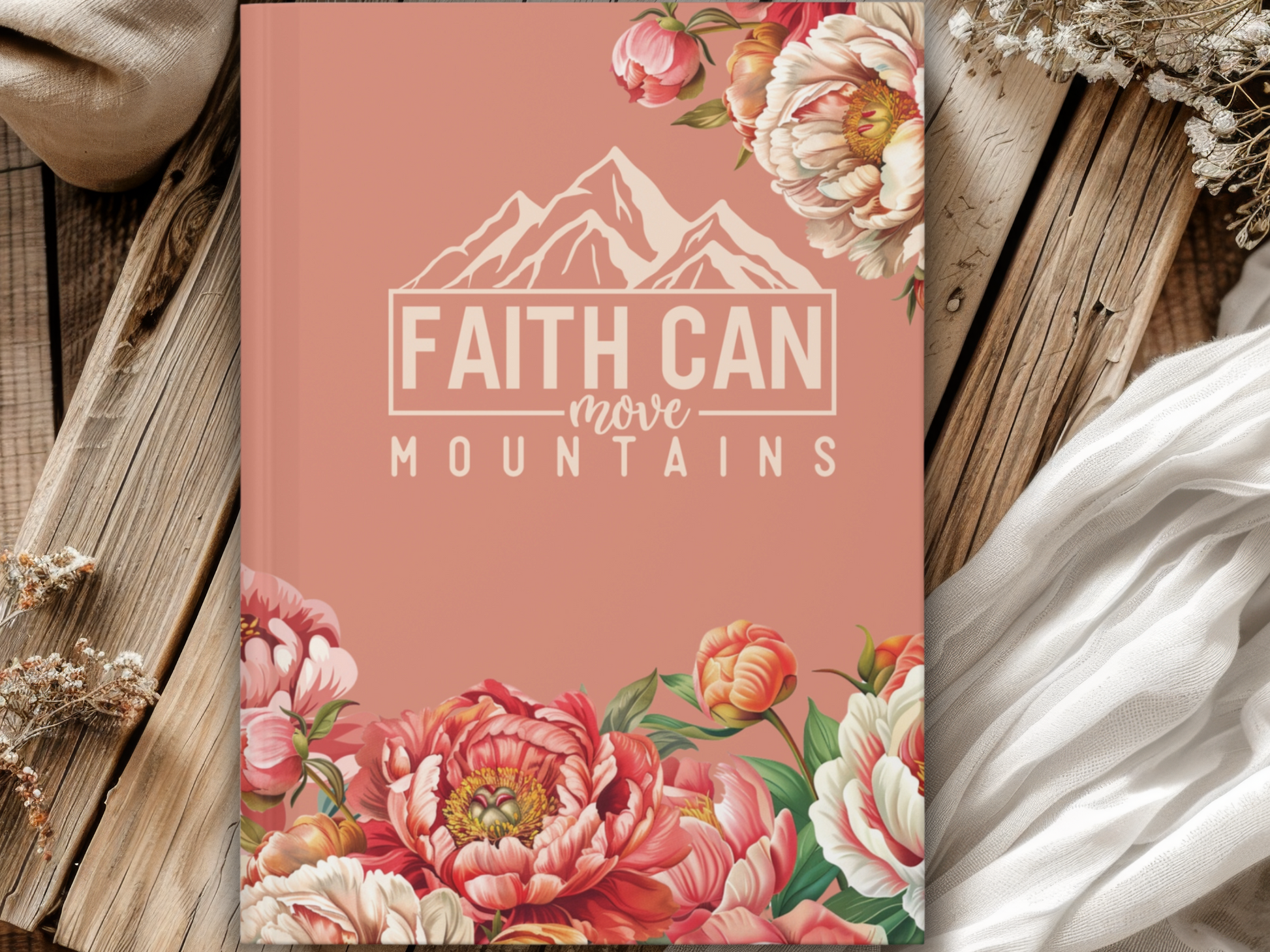 Cover of a beige book with floral designs and "Faith Can Move Mountains" text, placed on rustic wooden boards and surrounded by soft fabrics.