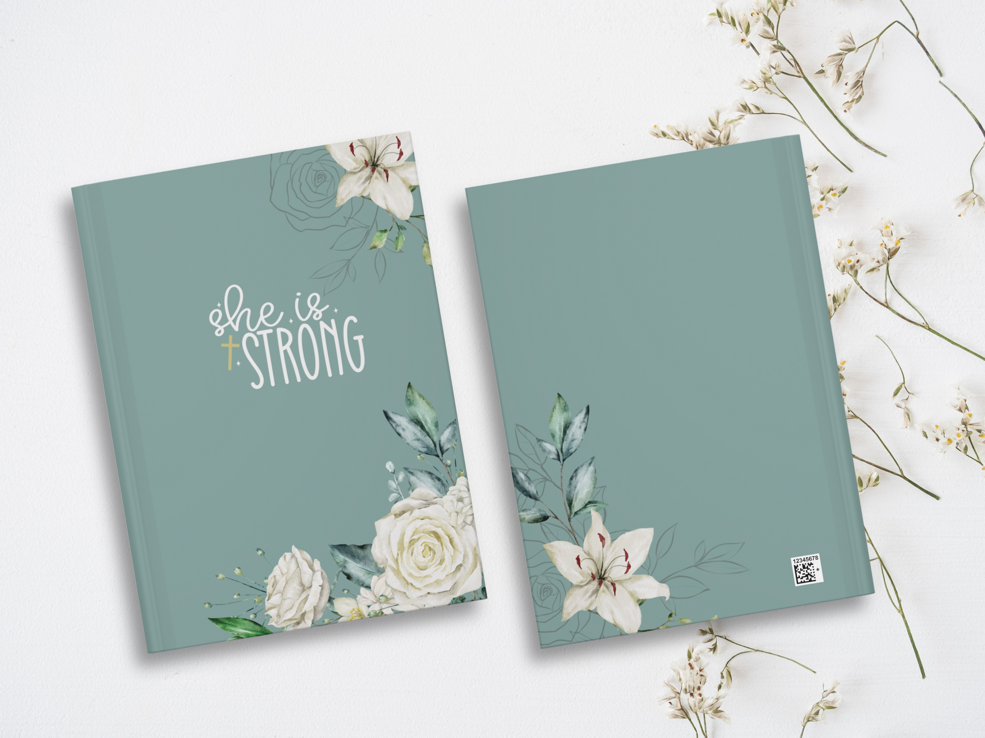 Two teal notebooks lie on a white surface, adorned with elegant white floral designs. One cover reads "She is Strong" in white script. Delicate flowers surround.