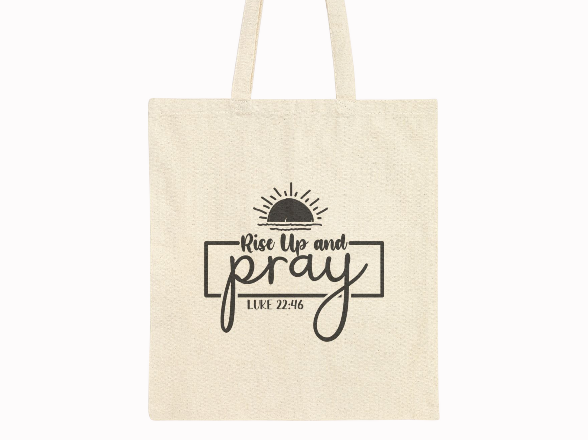 Beige tote bag with black text "Rise Up and Pray" beneath a half-sun graphic. The phrase "Luke 22:46" is displayed below, conveying a spiritual tone.