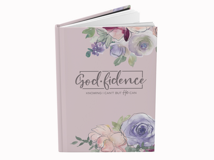 A book with a soft purple cover featuring watercolor flowers in pastel shades. The title "Godfidence" and subtitle "Knowing I Can't But He Can" are printed elegantly.