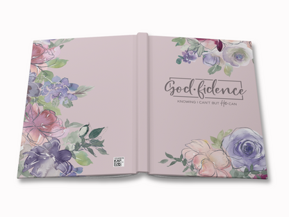 Open book with a light pink cover adorned with watercolor flowers in pink, purple, and green. Text reads "Godfidence: Knowing I can't, but He can." Calm, inspirational tone.