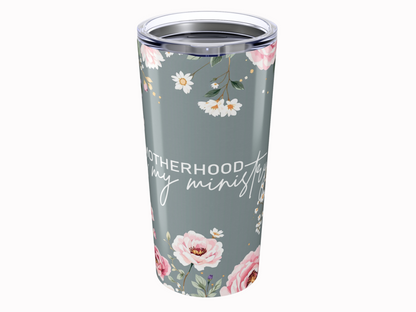 A floral tumbler with pink and white flowers on a grey background. Text reads "Motherhood is my ministry" in stylish script, conveying warmth.