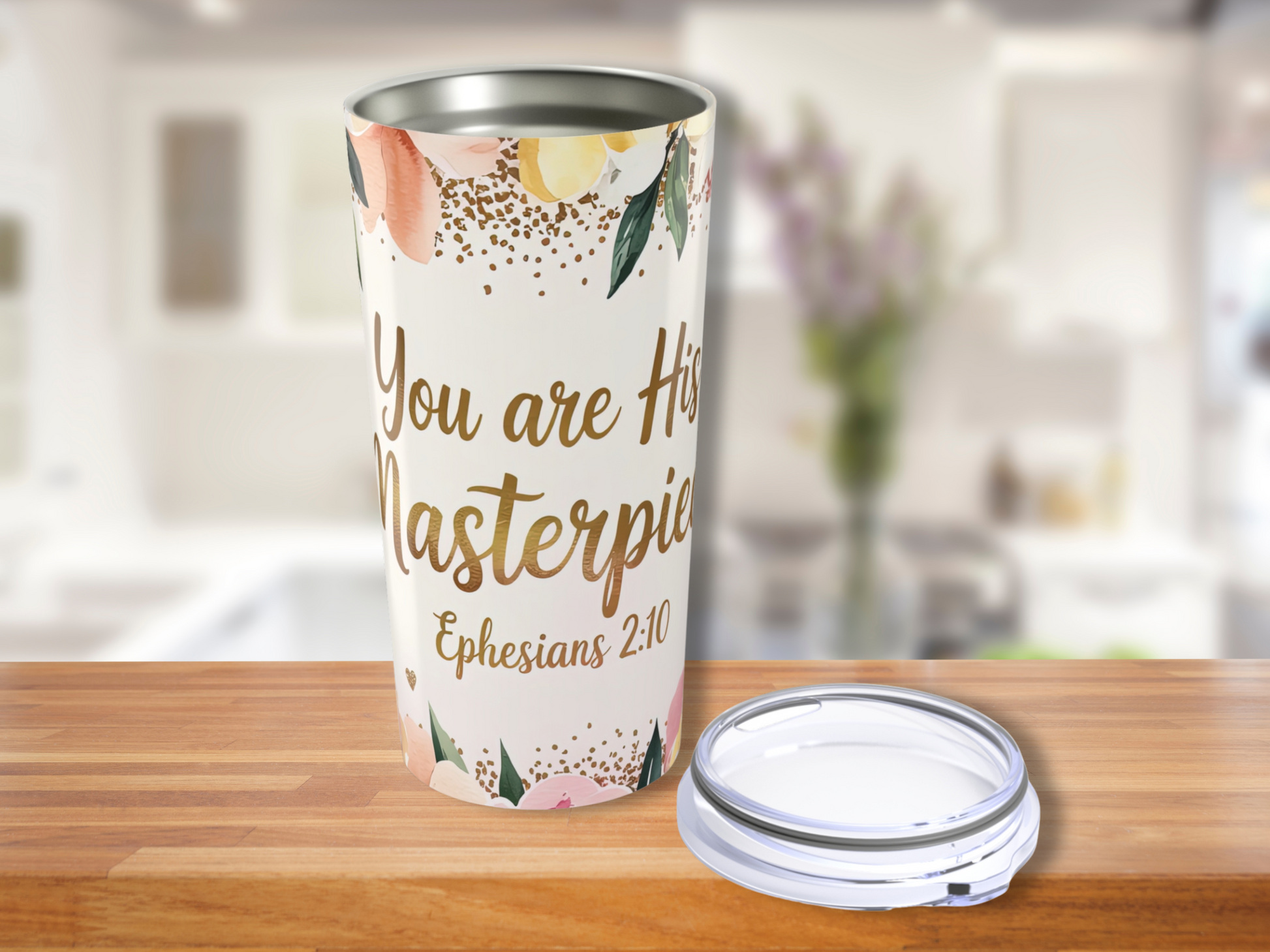 A floral Bible verse tumbler on a wooden surface displays "You are His Masterpiece, Ephesians 2:10" in elegant script. The setting is a softly blurred modern kitchen.
