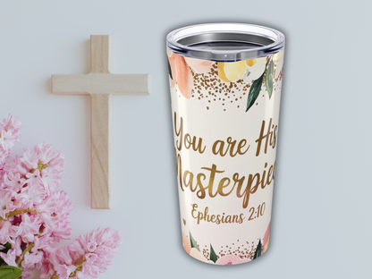 A wooden cross and pink flowers beside a Bible verse tumbler with floral design, displaying the text "You are His Masterpiece, Ephesians 2:10."