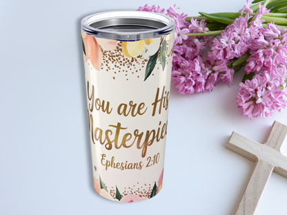A floral Bible verse tumbler with "You are His Masterpiece, Ephesians 2:10" in gold script. Near pink flowers and a wooden cross, evoking calm and inspiration.