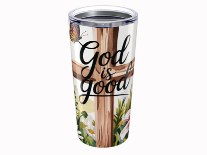 Tumbler with "God is good" text over a wooden cross. A butterfly and flowers add a serene, uplifting tone, blending nature and faith.