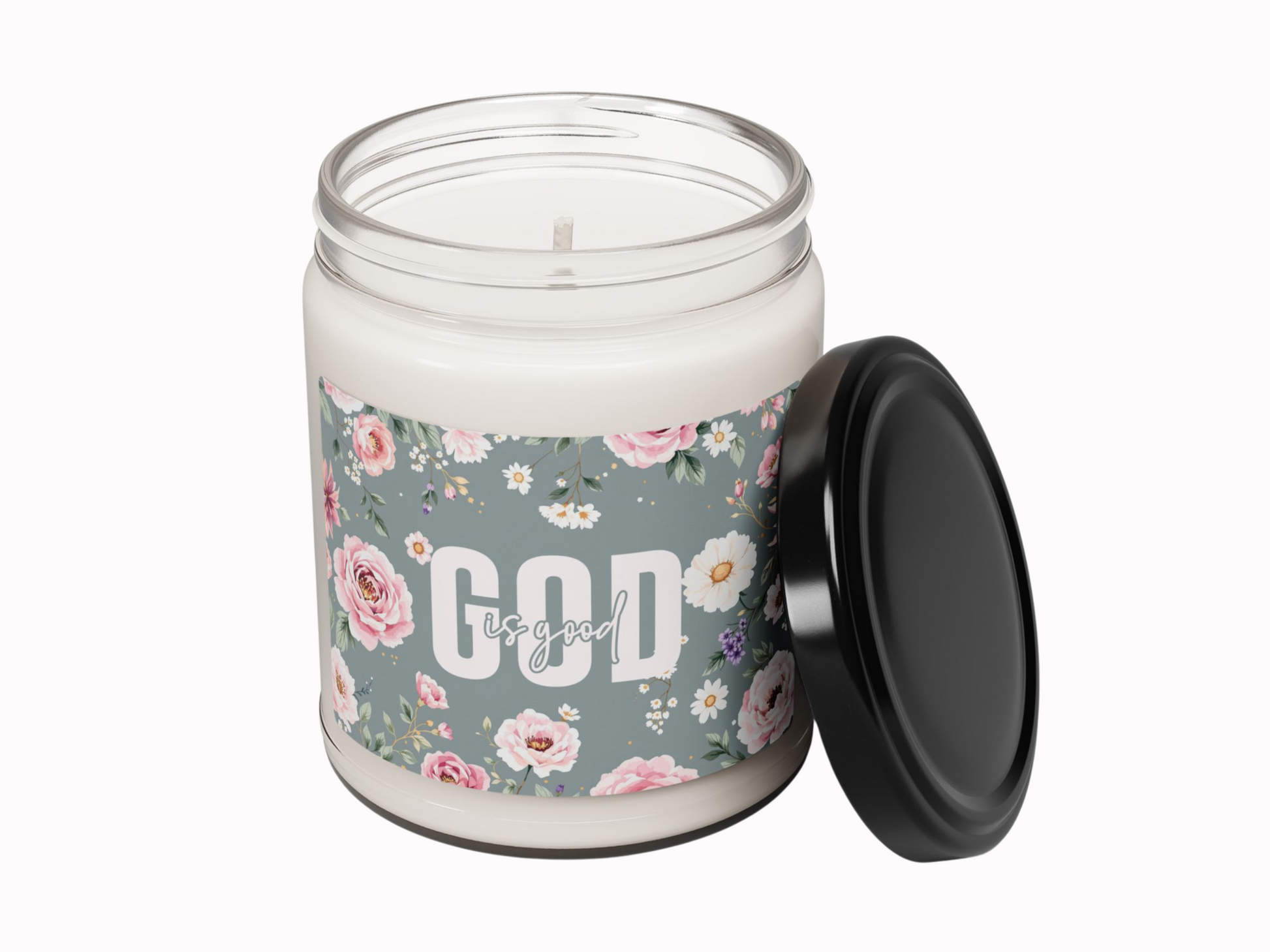 A glass jar candle with a floral label reads "God is good" in white text. The lid leans against the jar. The design conveys a peaceful, uplifting mood.
