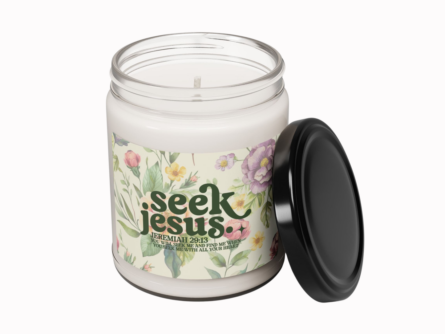 Glass biblical candle jar with a black lid placed beside it. The label shows floral illustrations and the words "Seek Jesus" with a quote from Jeremiah 29:13.