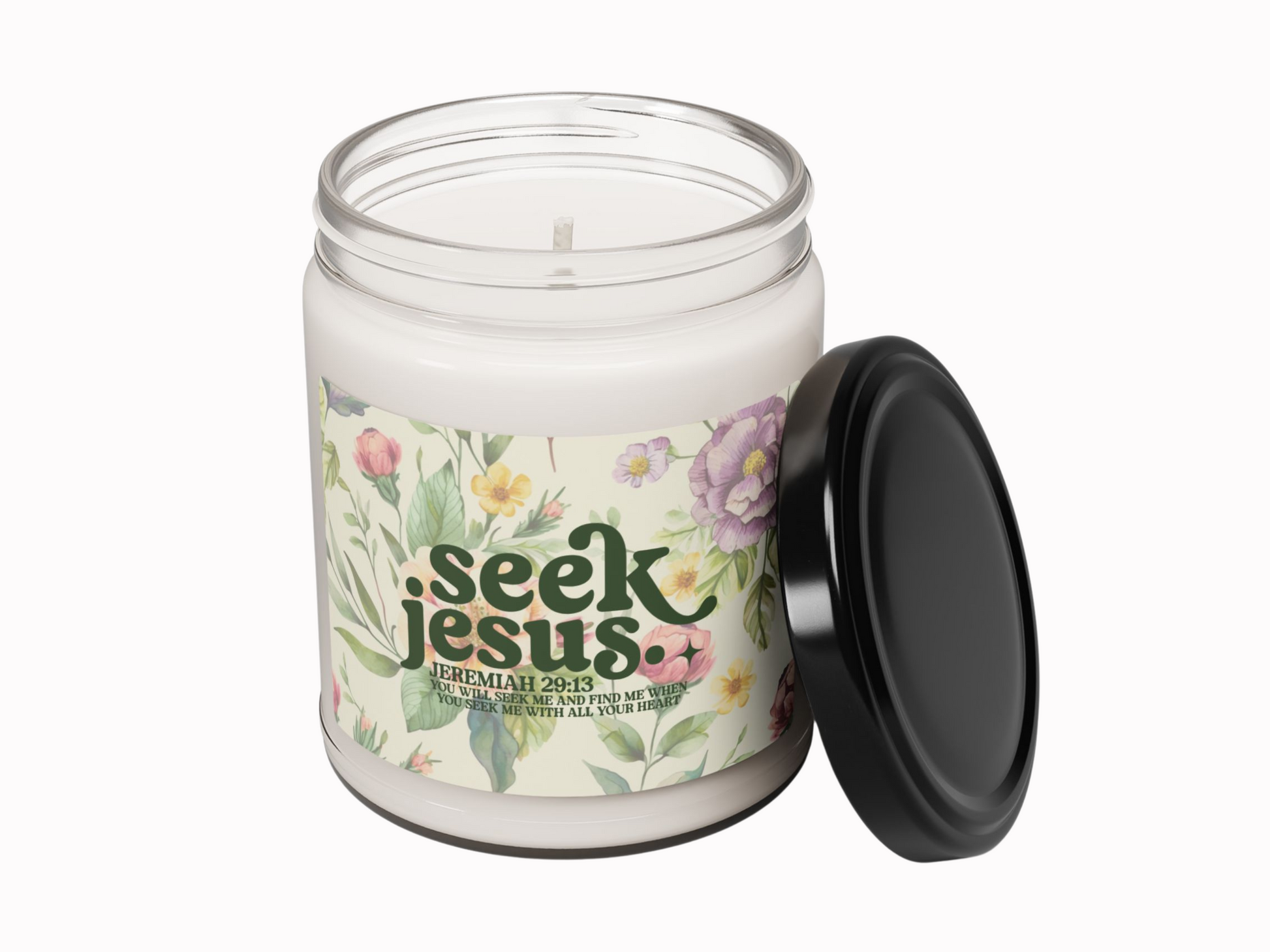 Glass biblical candle jar with a black lid placed beside it. The label shows floral illustrations and the words "Seek Jesus" with a quote from Jeremiah 29:13.