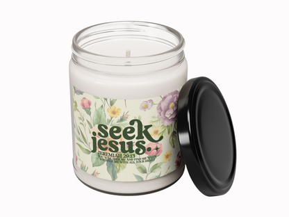 Glass biblical candle jar with a black lid placed beside it. The label shows floral illustrations and the words "Seek Jesus" with a quote from Jeremiah 29:13.