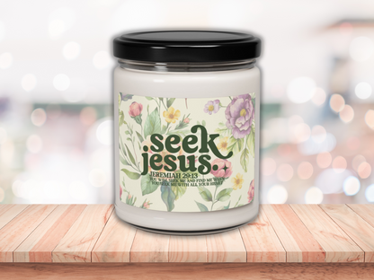 A soy candle with bible verse with a black lid on a wooden surface. The label reads "Seek Jesus" with floral designs, conveying peace and spirituality.