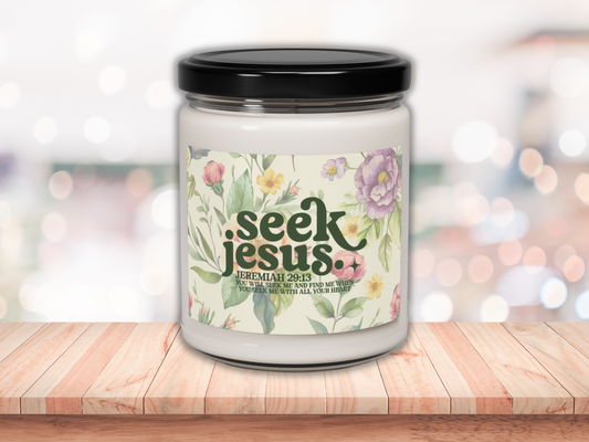 A soy candle with bible verse with a black lid on a wooden surface. The label reads "Seek Jesus" with floral designs, conveying peace and spirituality.