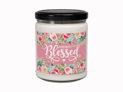 Glass jar candle with a black lid, featuring a floral label design. The pink label reads "Blessed" with "Jeremiah 17:7" in white script.