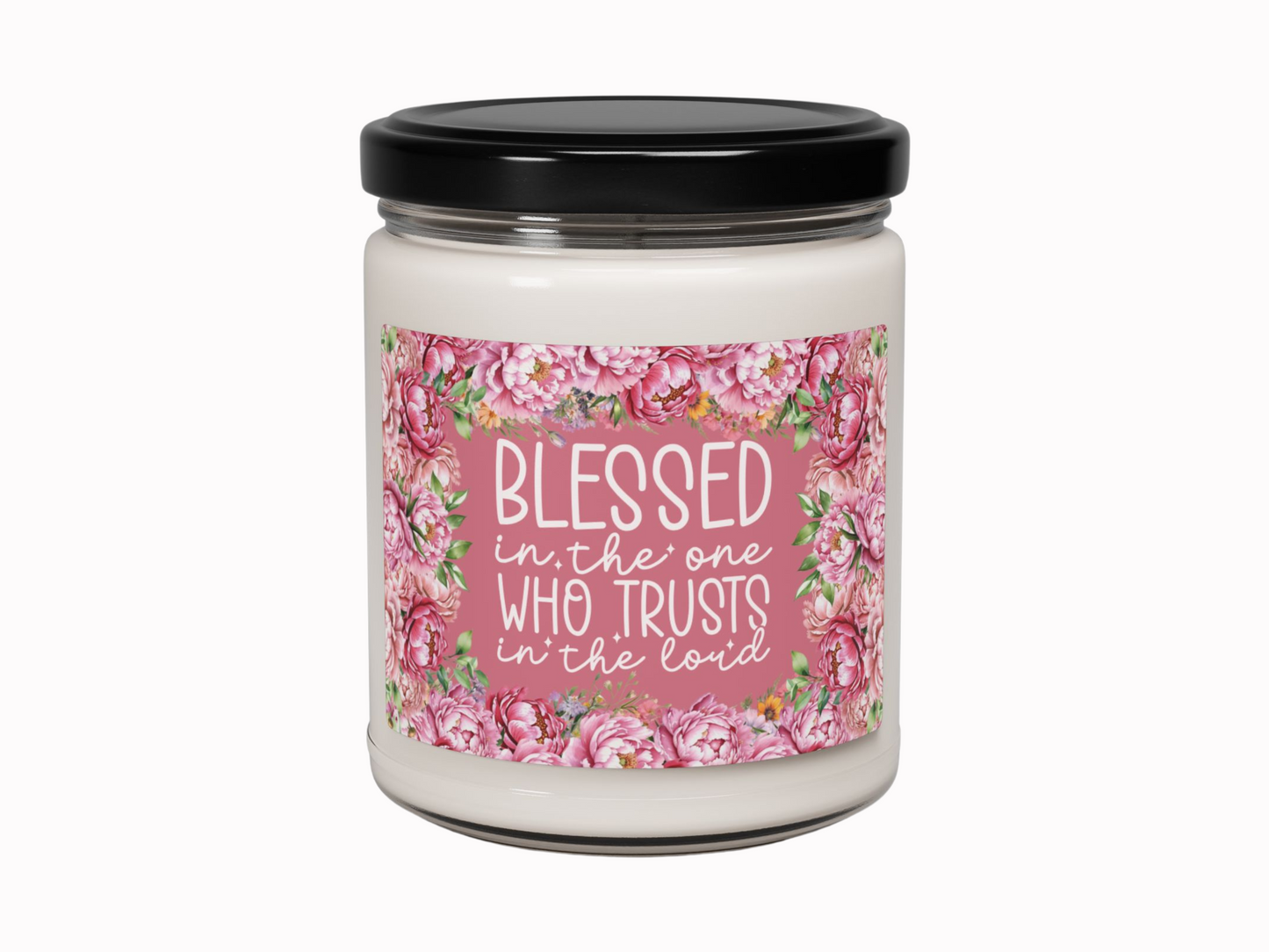 A white candle in a glass jar with a black lid. The label reads, "Blessed in the one who trusts in the Lord," surrounded by pink floral designs.