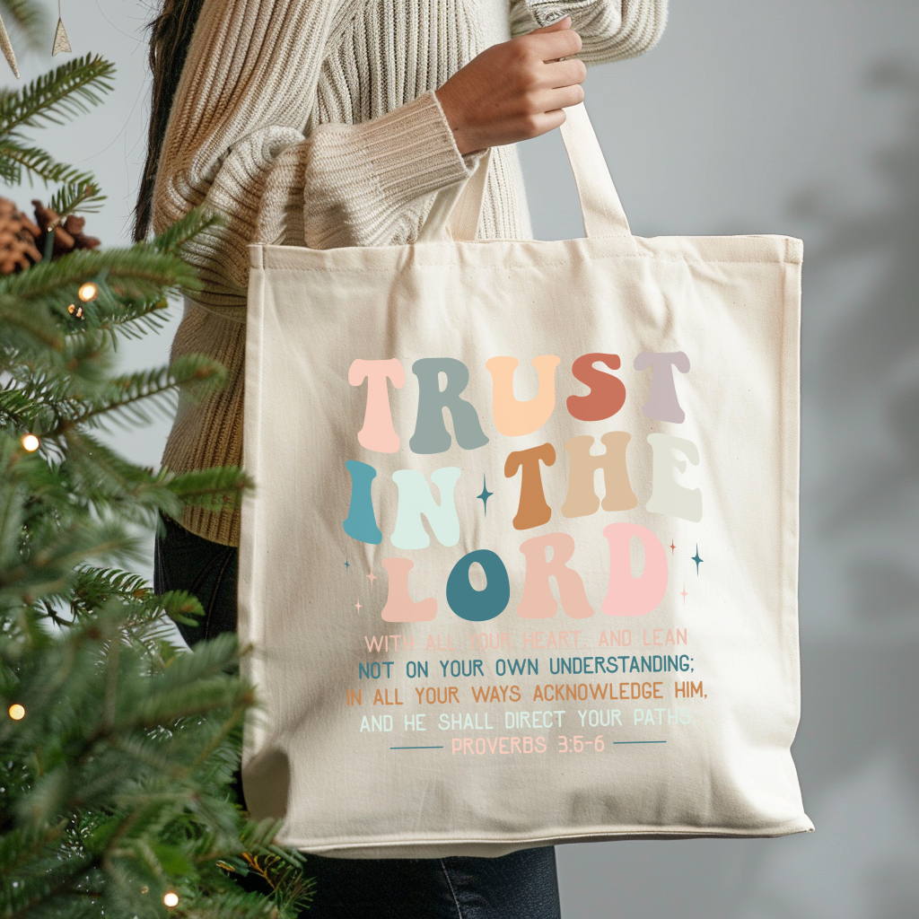 Tote bag with 'Trust in the Lord' text held by a person next to a Christmas tree.