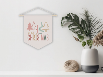 Decorative Christmas pennant flag with trees and 'Merry Christmas' text, placed on a white surface with plants and a vase.