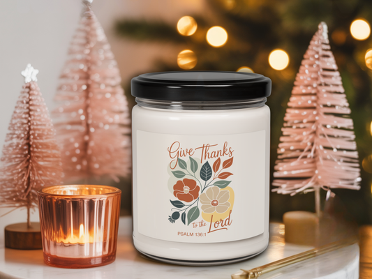 Candle with 'Give Thanks to the Lord' label in a festive setting with Christmas trees and lights.