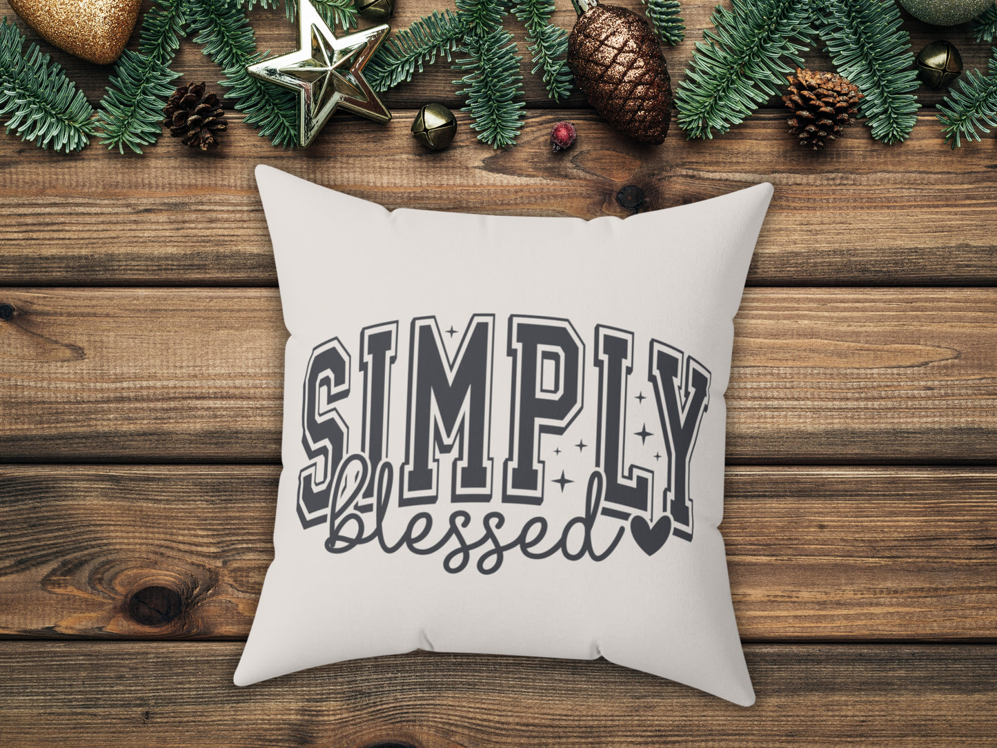 White pillow with 'Simply Blessed' text on a wooden surface with Christmas decorations.