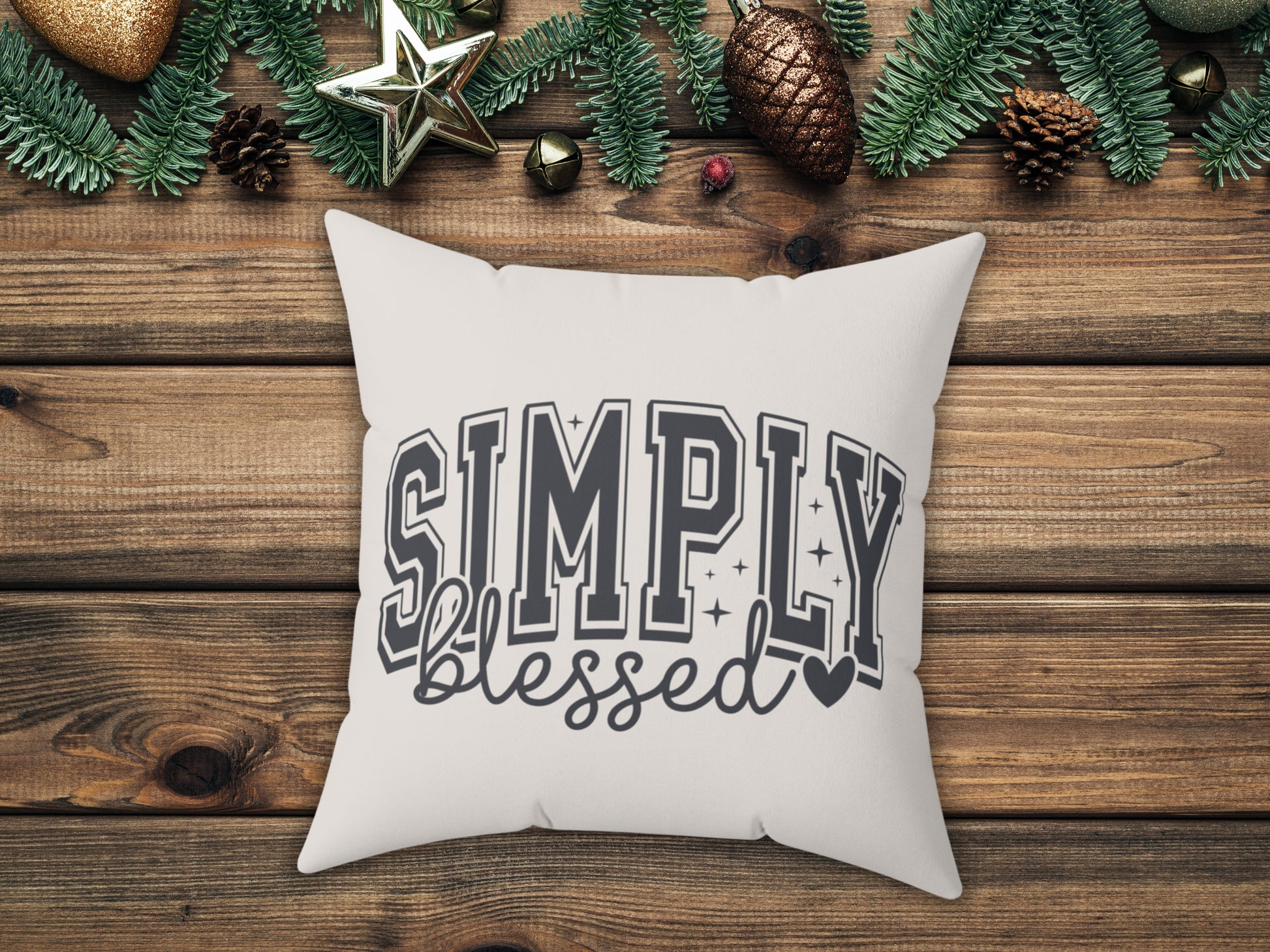 White pillow with 'Simply Blessed' text on a wooden surface with Christmas decorations.