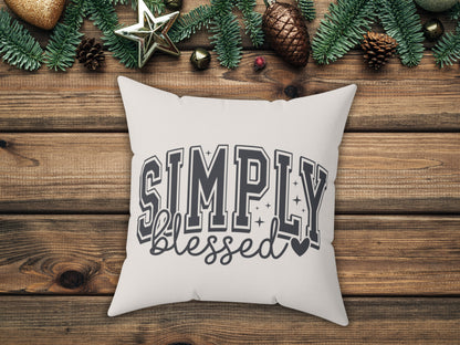 White pillow with 'Simply Blessed' text on a wooden surface with Christmas decorations.