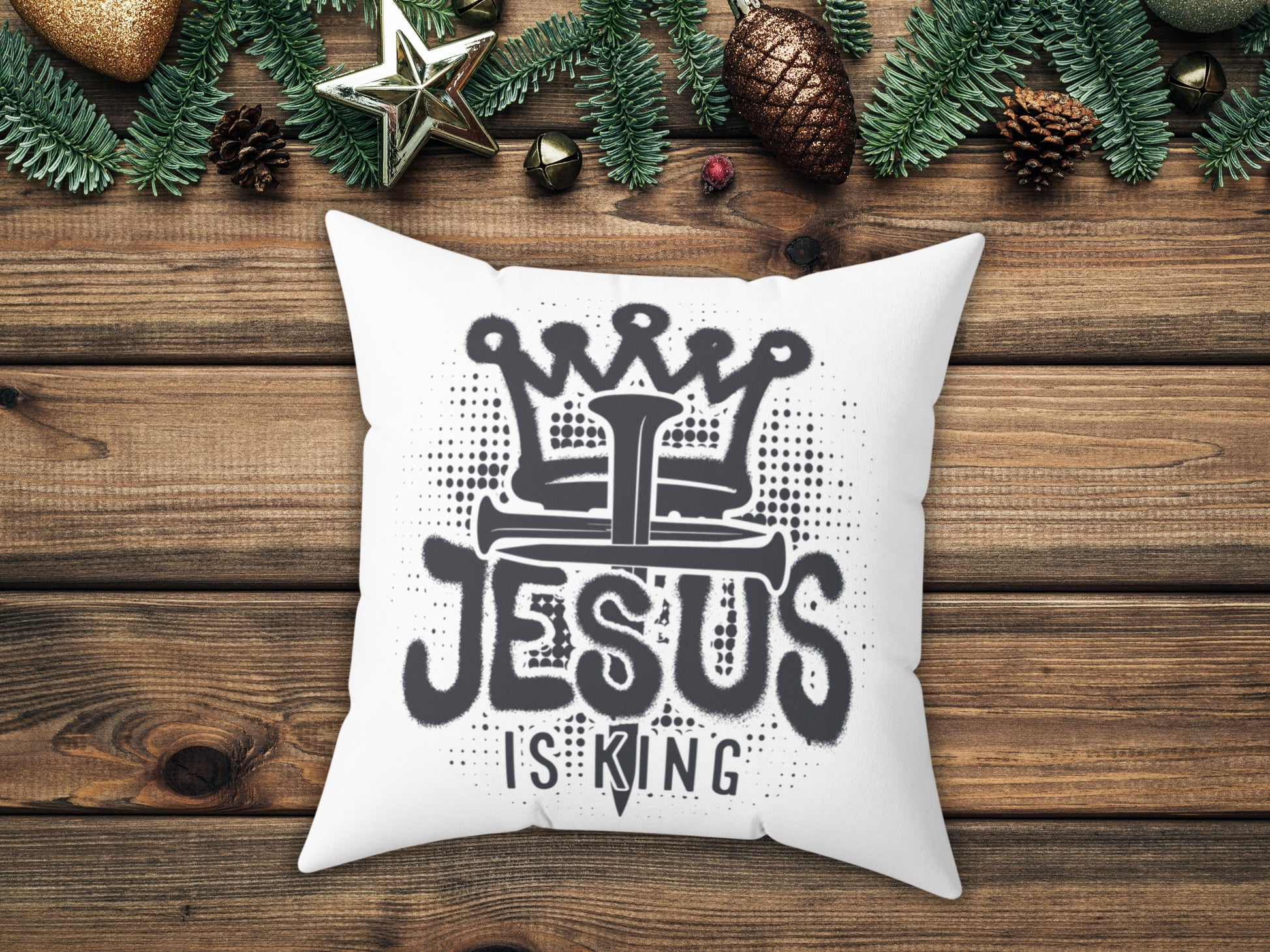 White pillow with 'Jesus is King' design on a wooden surface with Christmas decorations.