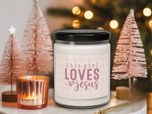 Candle jar with 'this girl loves Jesus' text in a festive setting with Christmas trees and lights.