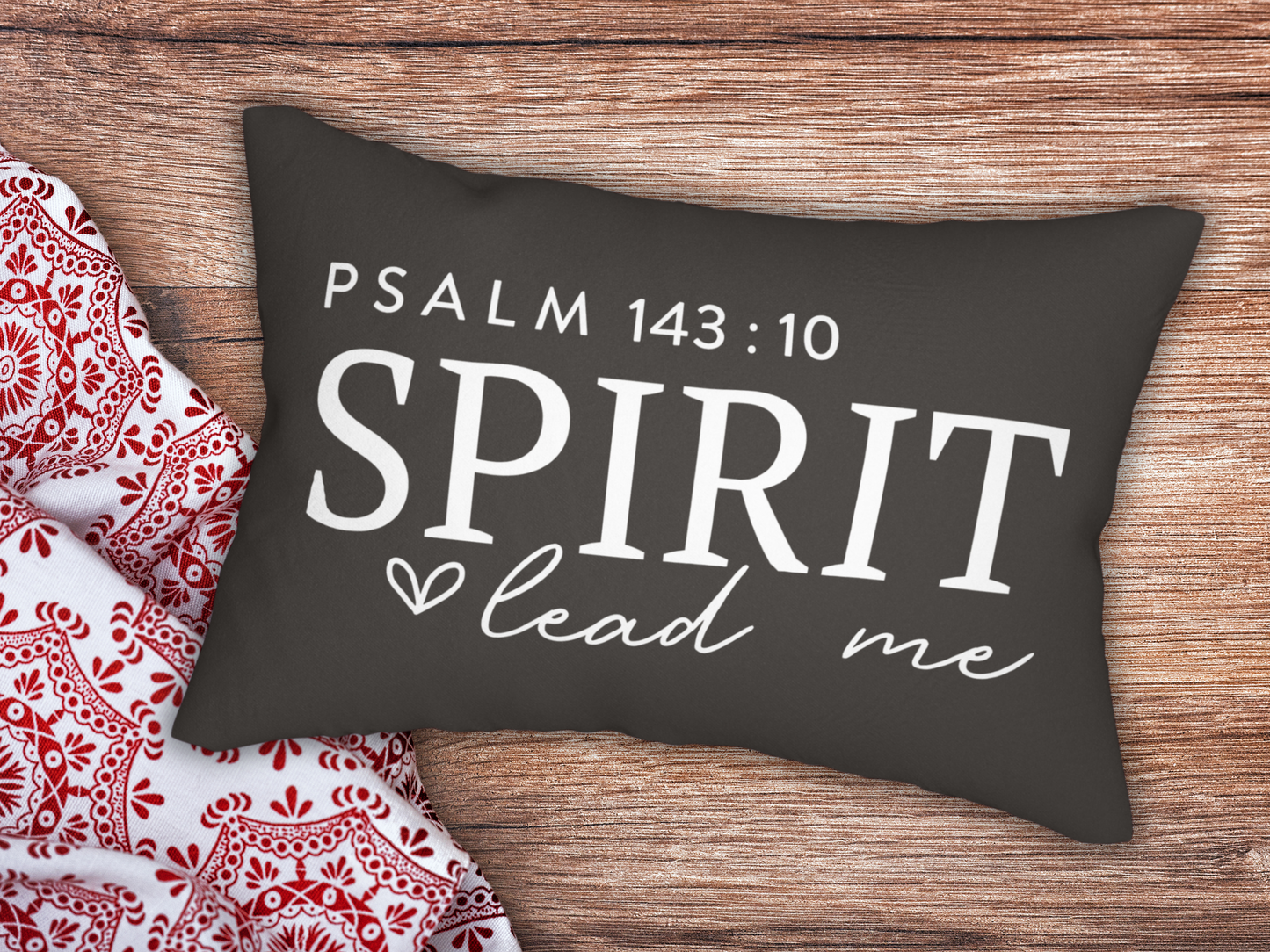 Decorative pillow with 'Psalm 143:10 Spirit lead me' text on a wooden surface with a red and white patterned fabric.