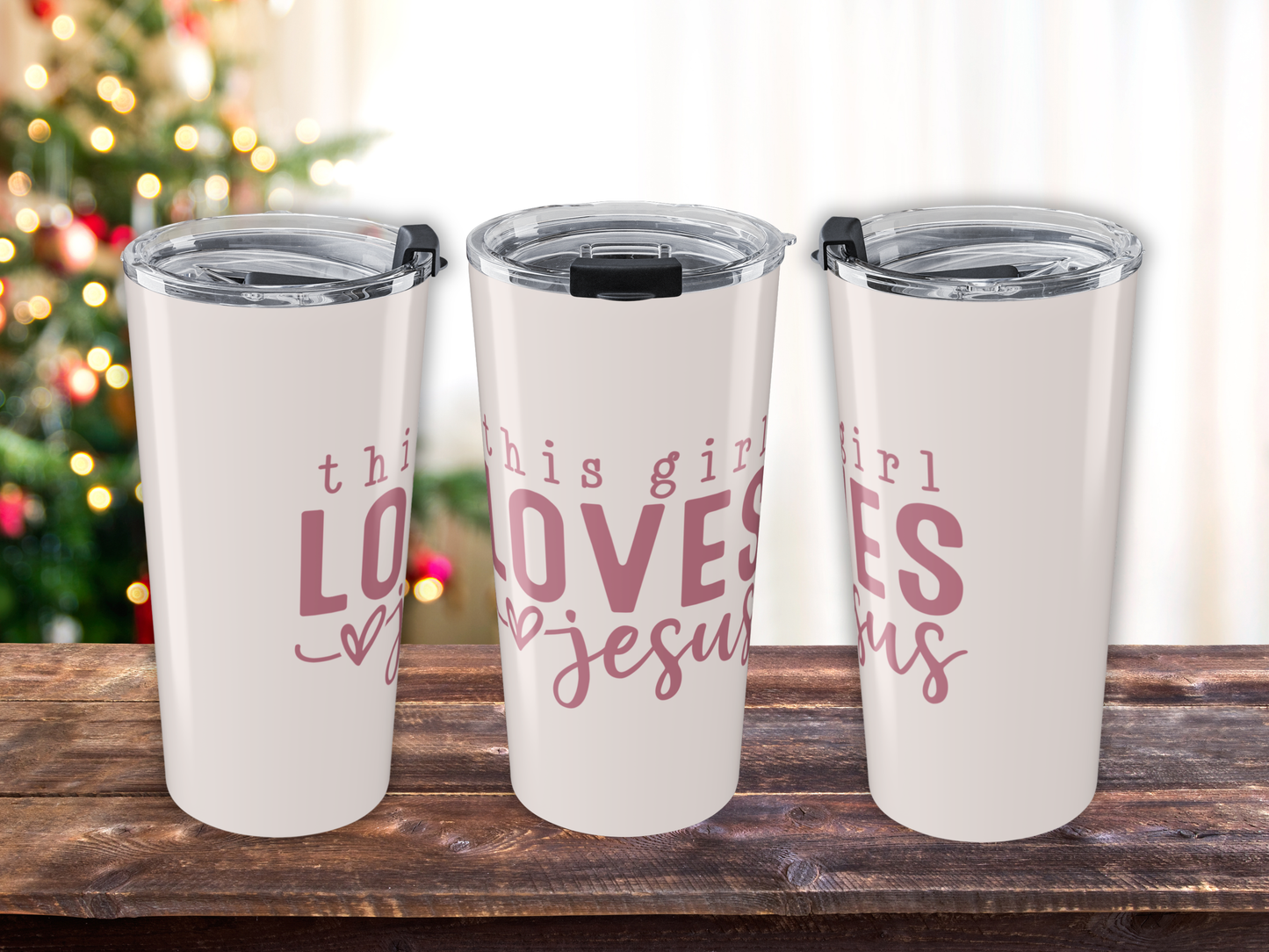 Three insulated tumblers with pink text on a wooden surface with a blurred Christmas tree in the background.