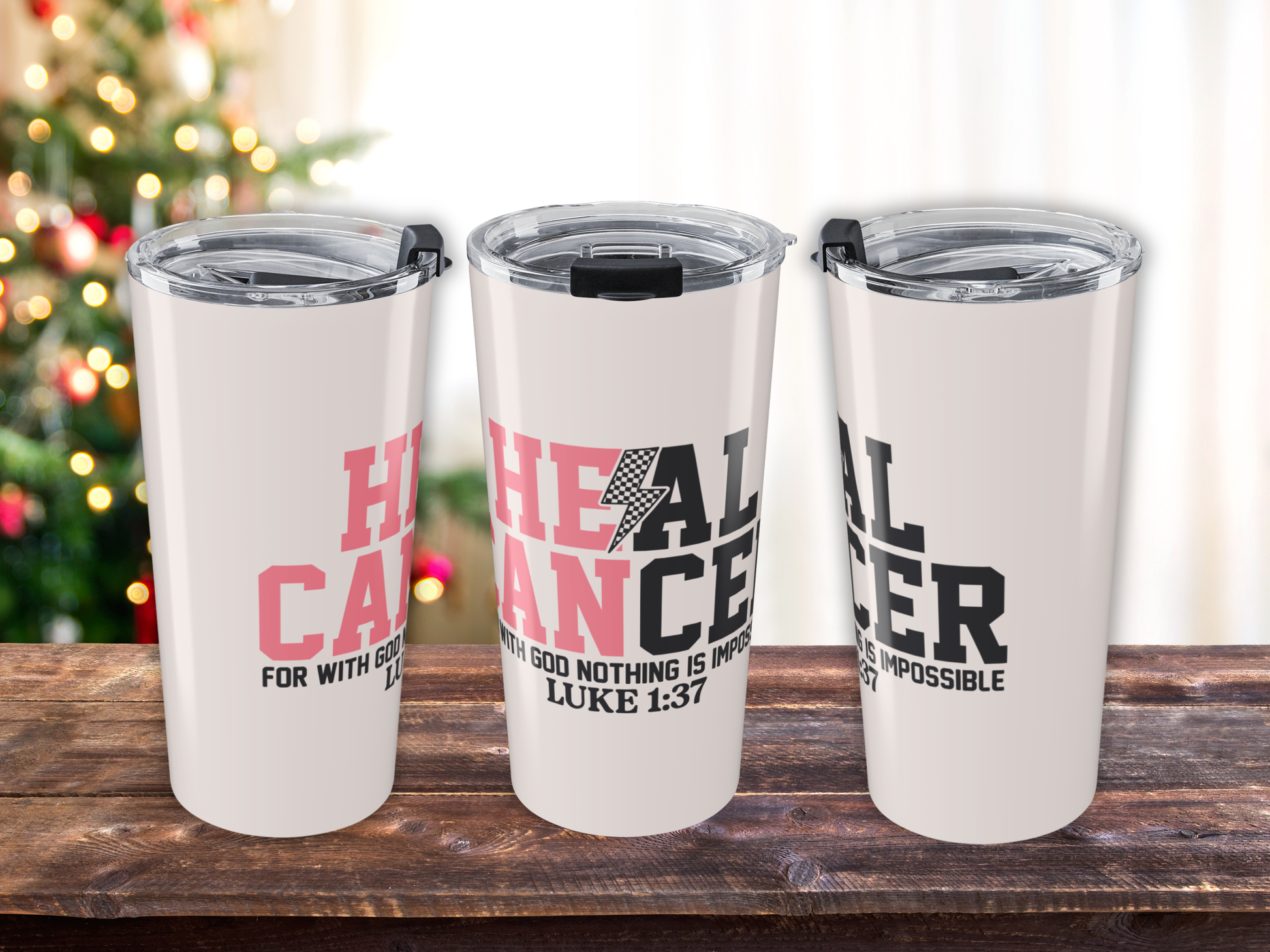 Three pink tumblers with motivational text on a wooden surface with a blurred Christmas tree in the background.