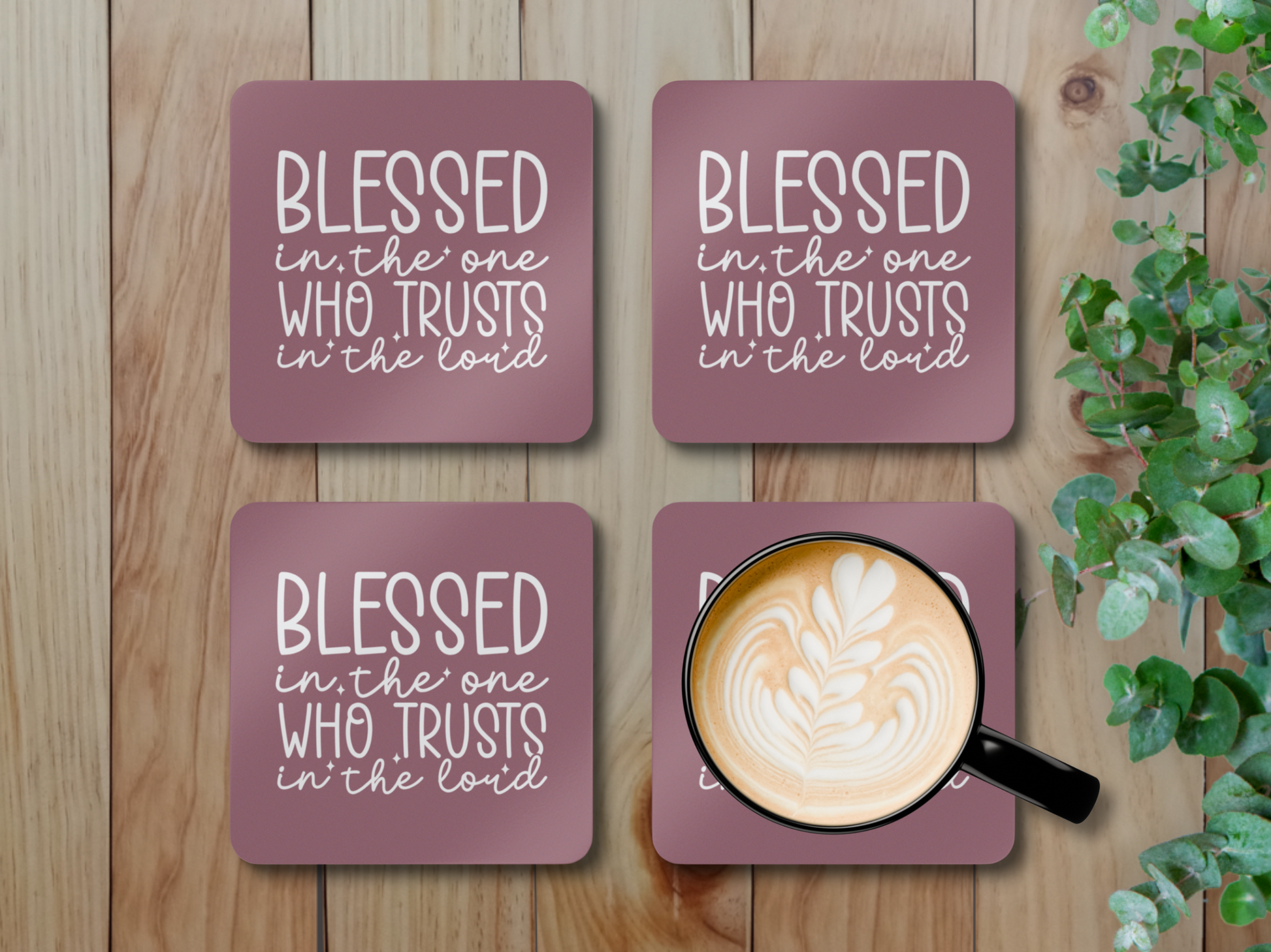 Set of four coasters on a wooden surface with greenery, one holding a latte in a black cup.