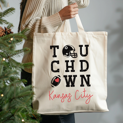 Tote bag with 'Touchdown Kansas City' text held by a person next to a Christmas tree.
