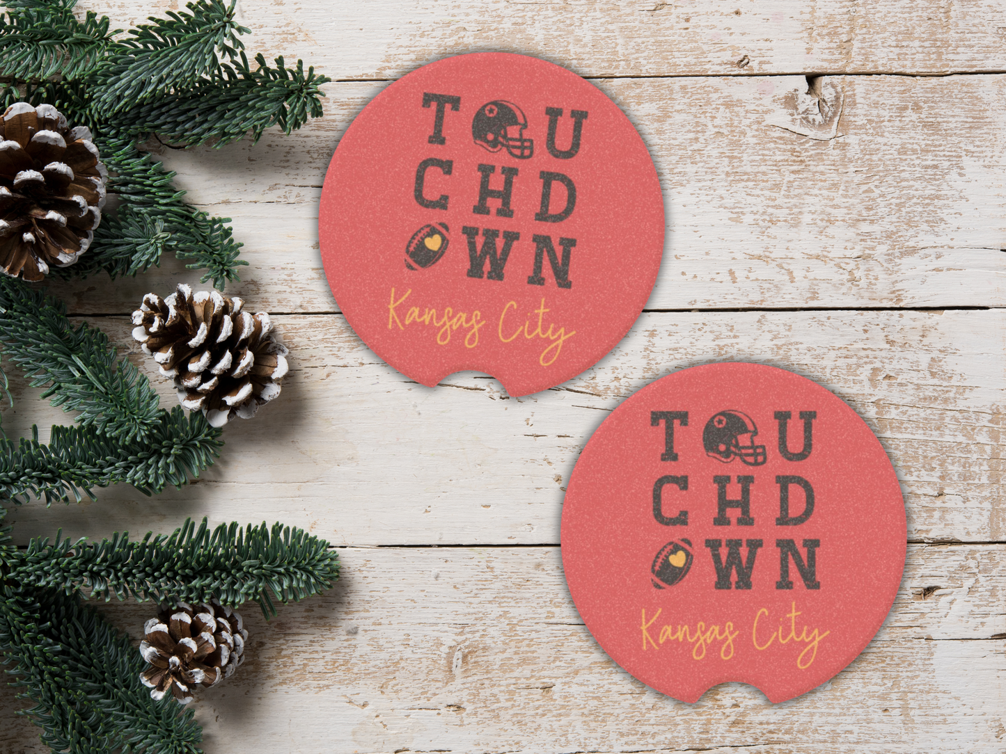 Two red 'Touchdown Kansas City' coasters on a wooden surface with pine cones and greenery.