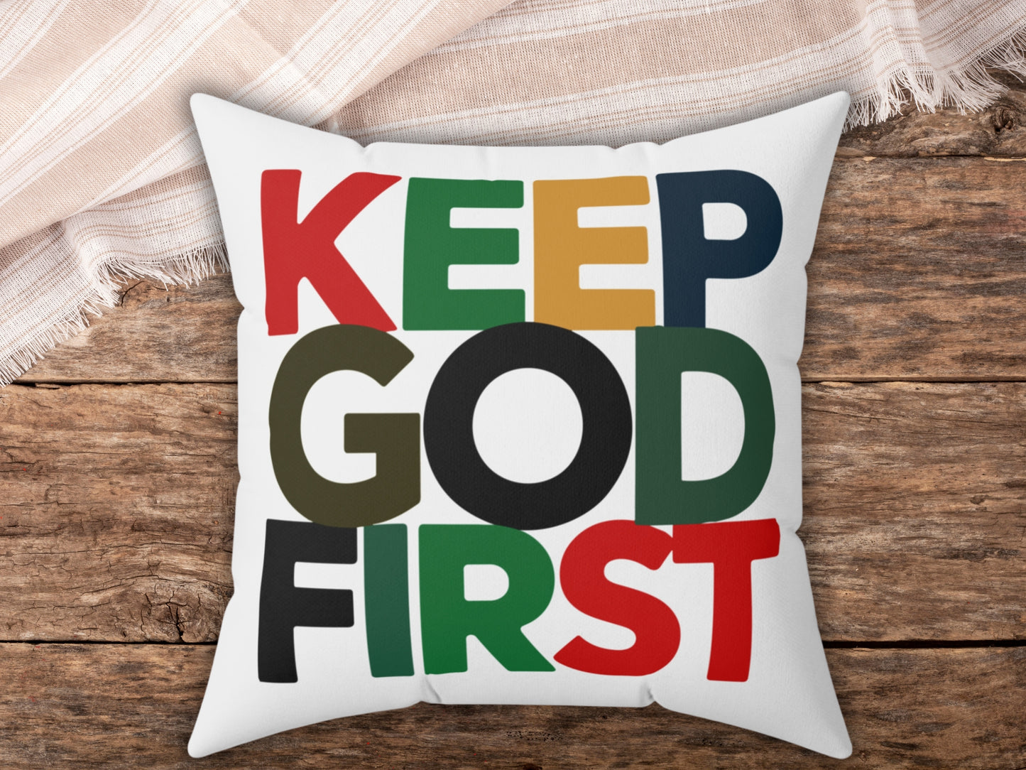 Pillow with 'KEEP GOD FIRST' text in colorful letters on a wooden surface.
