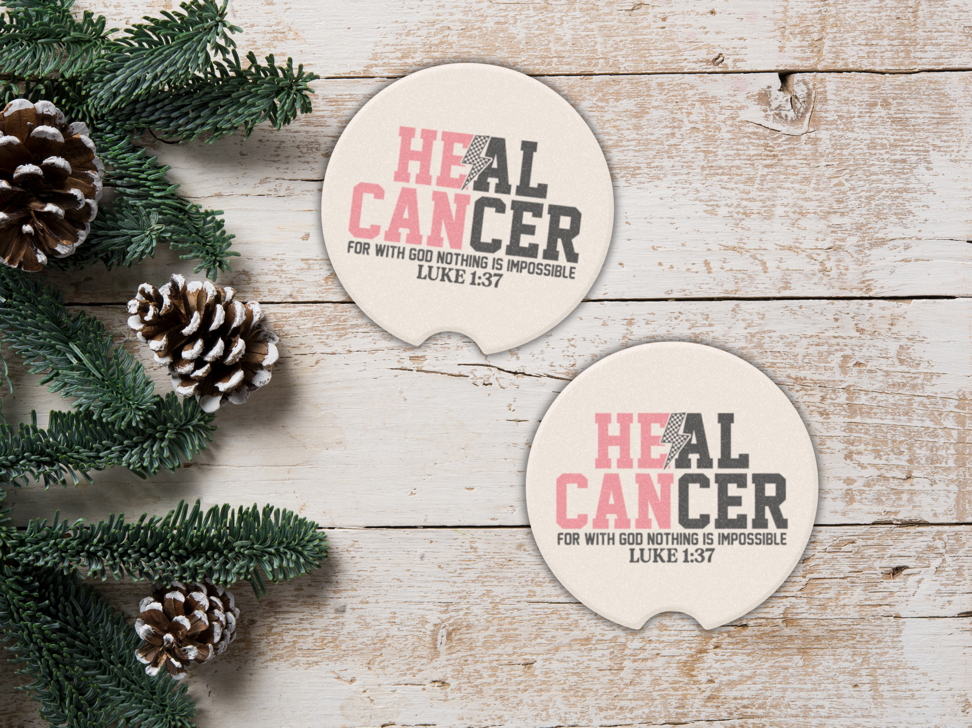 Two 'Heal Cancer' coasters on a wooden surface with pine cones and greenery.