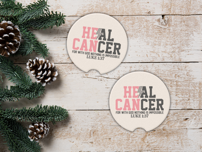 Two 'Heal Cancer' coasters on a wooden surface with pine cones and greenery.