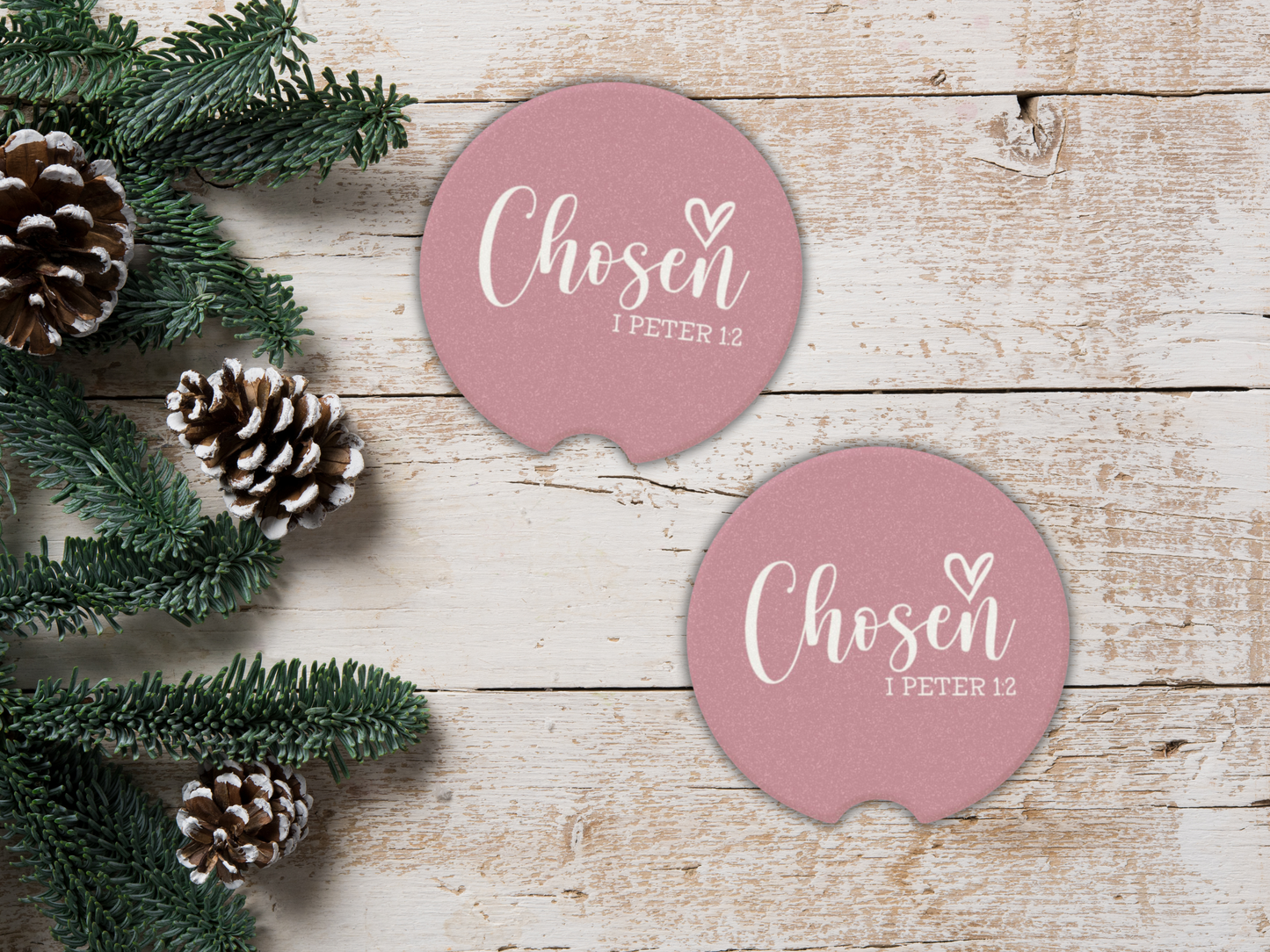 Pink coasters with 'Chosen 1 Peter 1:2' text on a wooden surface with pine cones and greenery.