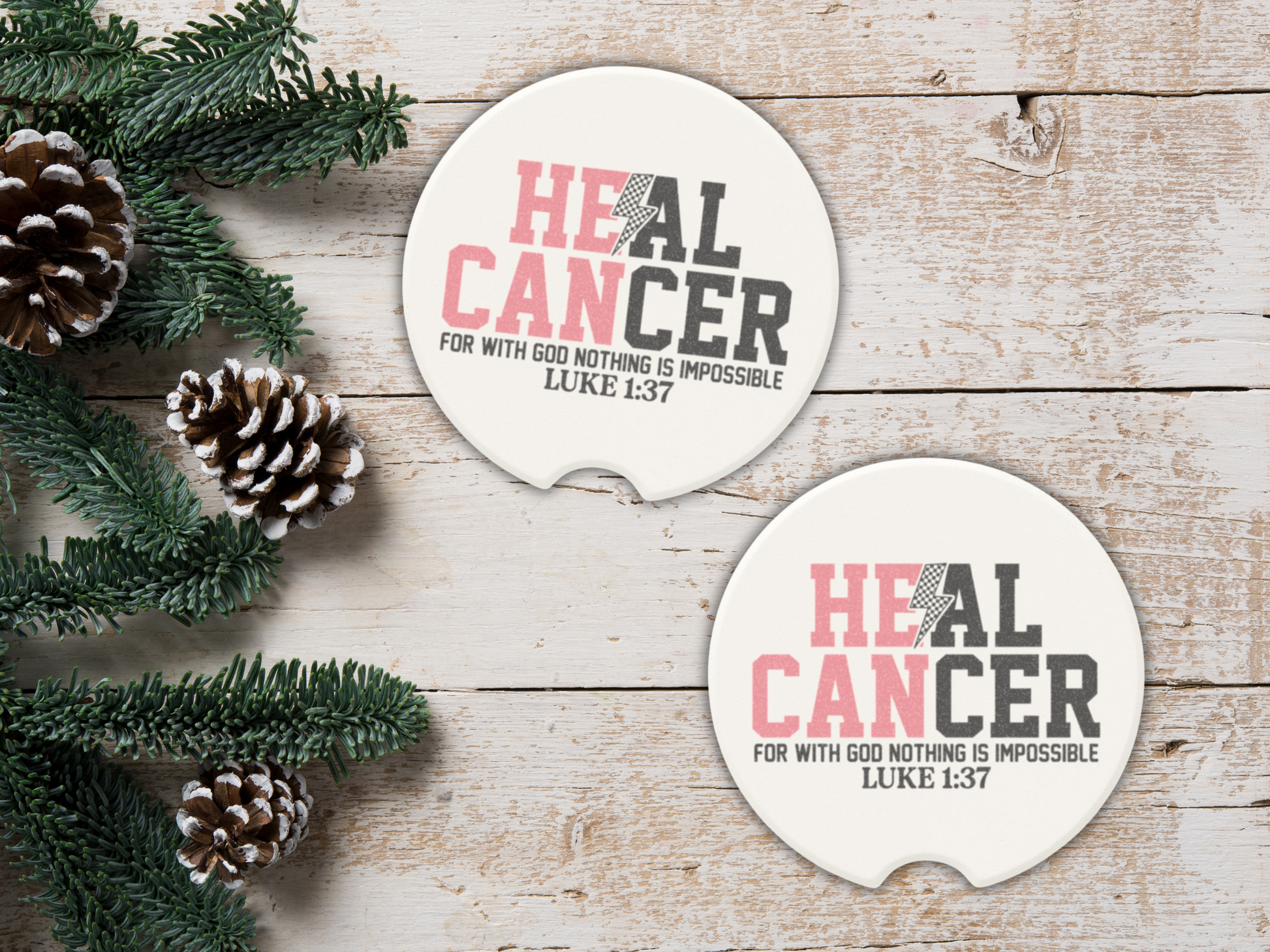 Two 'Heal Cancer' coasters on a wooden surface with pine cones and greenery.