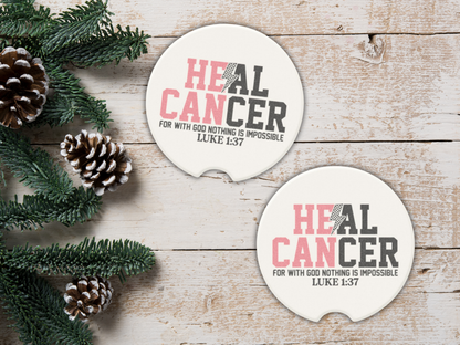Two 'Heal Cancer' coasters on a wooden surface with pine cones and greenery.