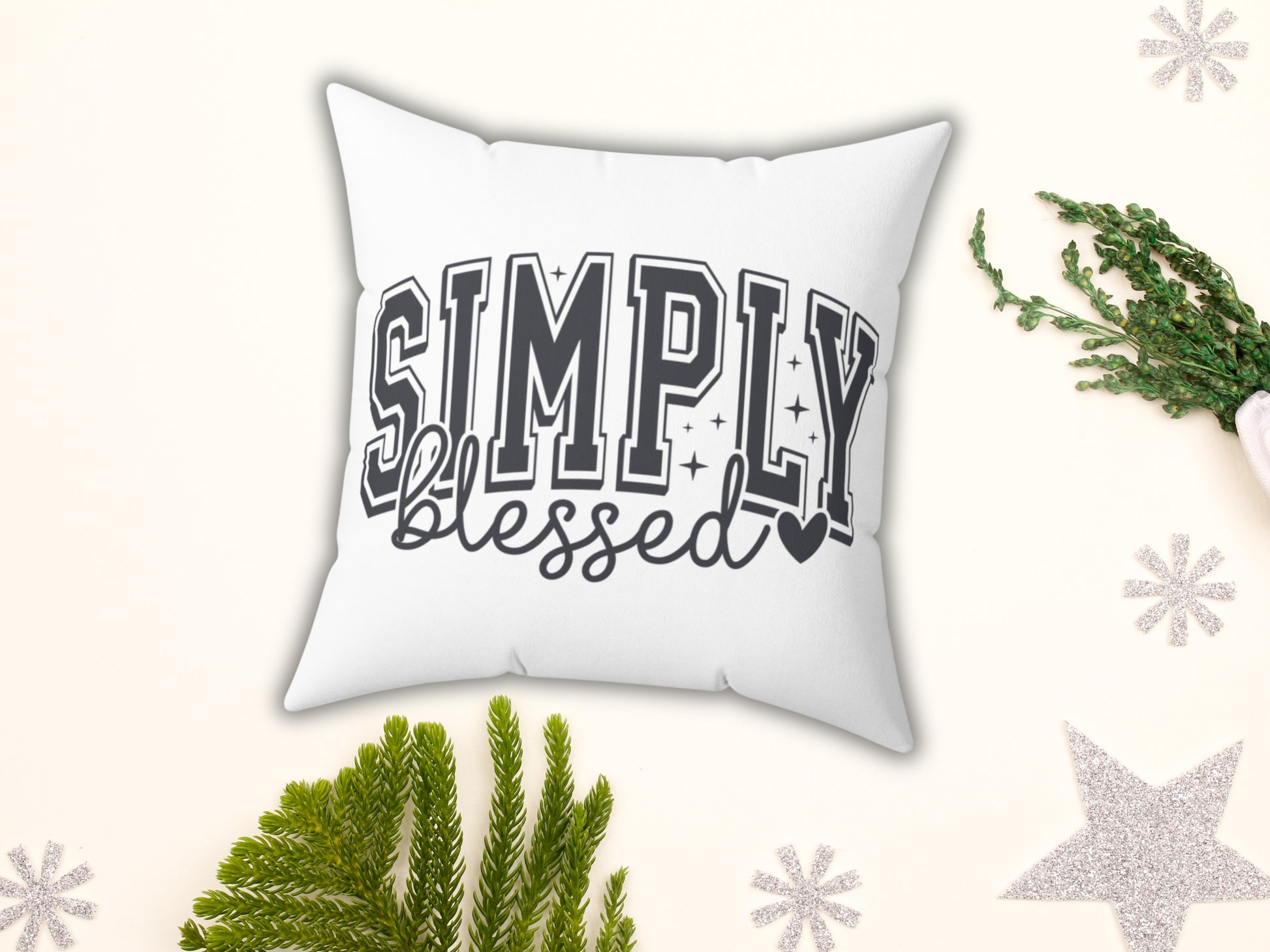 White pillow with 'Simply Blessed' text on a decorative background with greenery and snowflakes.