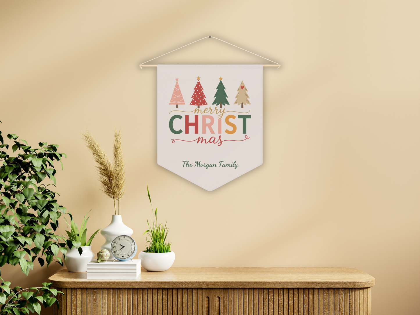 Decorative Christmas banner with colorful trees on a beige wall above a wooden cabinet.