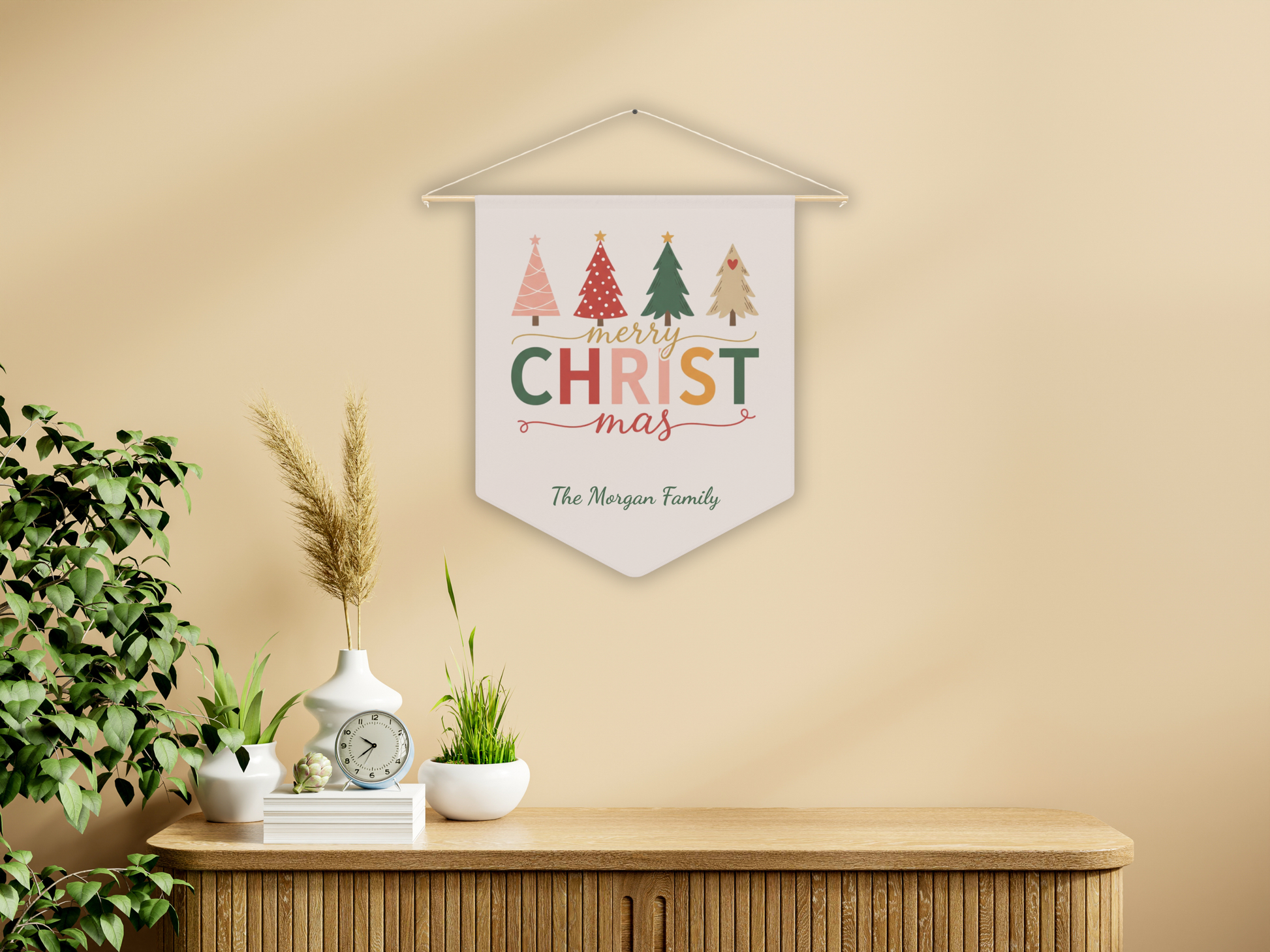 Decorative Christmas banner with colorful trees on a beige wall above a wooden cabinet.