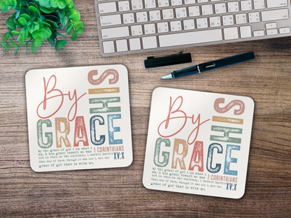 Pair of scripture coasters with “By His Grace” design styled on a wooden desk with keyboard, pen, and greenery.