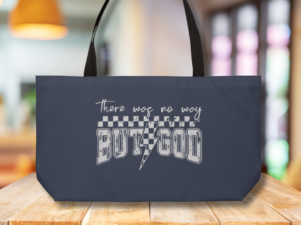 Navy blue tote bag on a wooden table, featuring white distressed text “There was no way BUT GOD” with checkerboard and lightning bolt design.