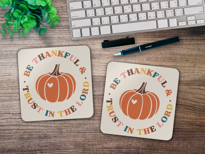 Two “Be Thankful & Trust in the Lord” coasters styled on wooden desk with keyboard, pen, and plant.