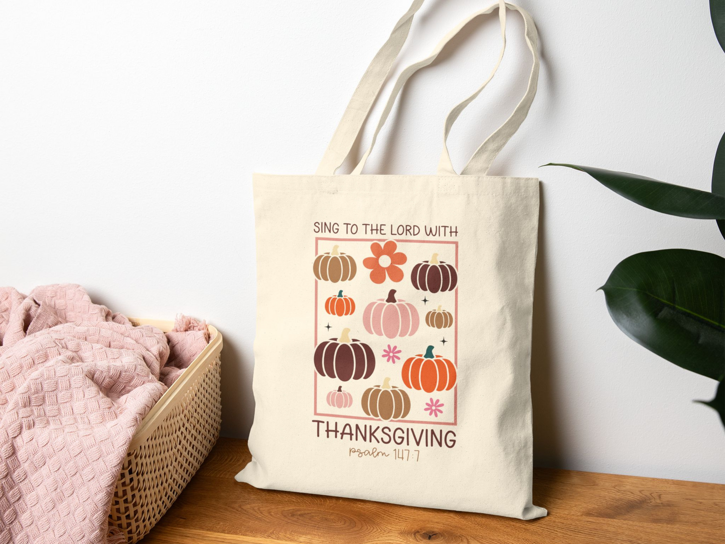 Tote bag on a rustic white background styled with a cozy sweater, pinecone, candle, and autumn leaves.